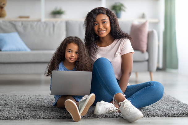 Distance education concept. Happy black mom and her cute little daughter watching online lesson on laptop at home - Foto, Bild