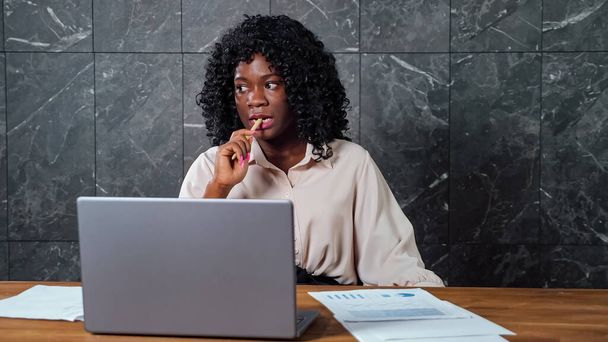 Задумчивая черная деловая женщина смотрит вокруг, держа ручку - Фото, изображение