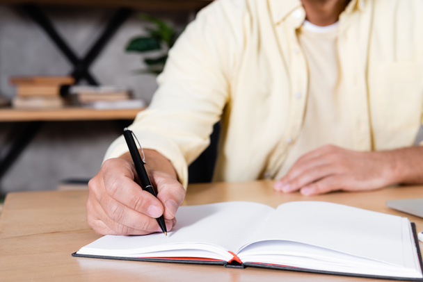 partial view of man writing in notebook while working at home, blurred background - Photo, Image