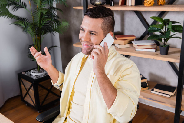smiling man gesturing while talking on smartphone at home - Fotografie, Obrázek