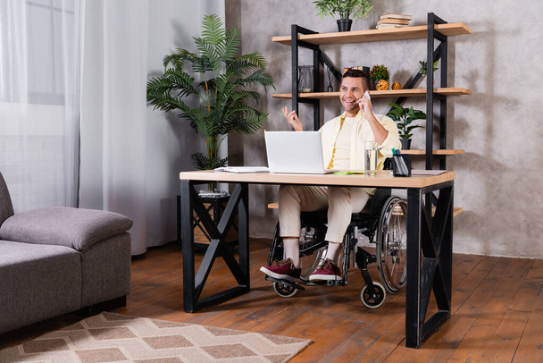 fröhlicher behinderter Mann gestikuliert während er im Home Office mit dem Smartphone spricht - Foto, Bild