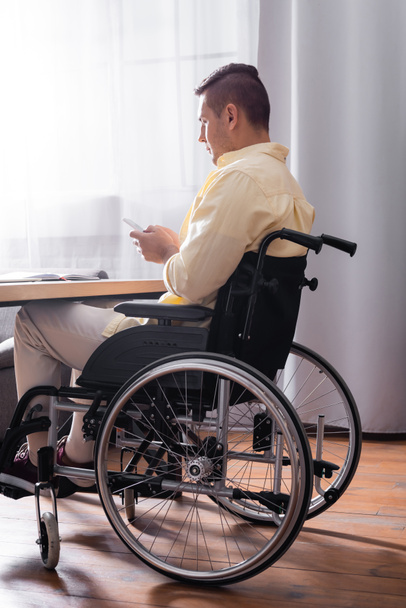 man in wheelchair messaging on mobile phone while working in office - 写真・画像