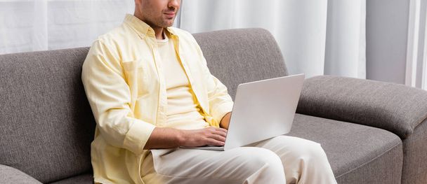 Kanepede oturan ve dizüstü bilgisayarda, afişte yazan serbest çalışanın kısmi görüntüsü - Fotoğraf, Görsel