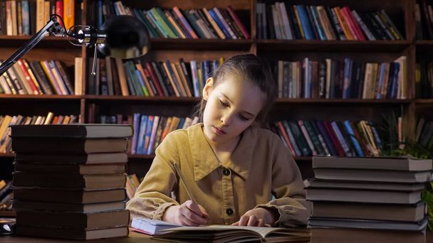 Chica concentrada en chaqueta escribe tarea en cuaderno - Foto, imagen