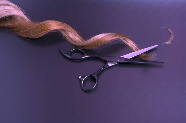 Tijeras profesionales negras abiertas con hebra de pelo rizado sobre fondo oscuro, tijeras de peluquería - Foto, imagen