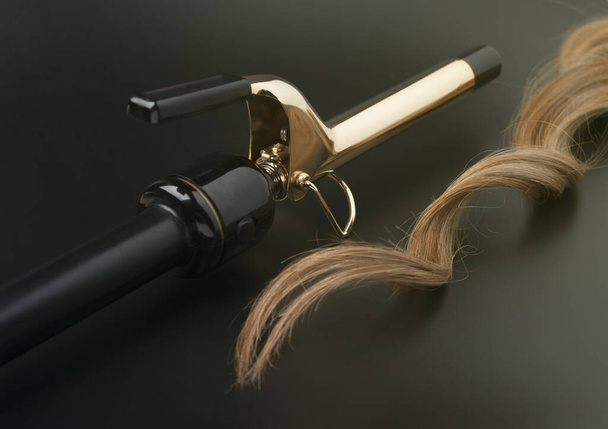 Offene schwarze Profi-Schere mit Strähne aus lockigem Haar auf dunklem Hintergrund, Friseurschere - Foto, Bild