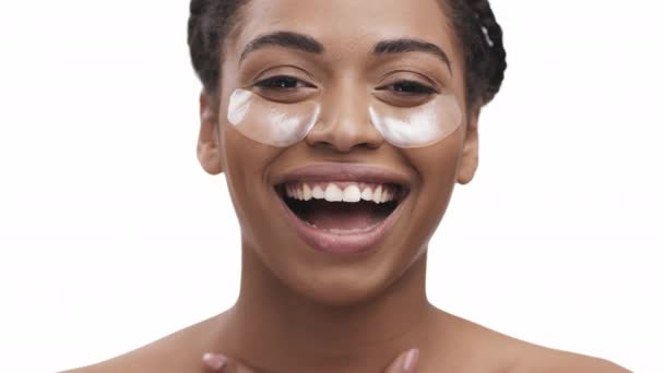 Piękno i pielęgnacja skóry. Portret szczęśliwej Afroamerykanki z plastrami przeciwzmęczeniowymi pod oczami śmiejącej się do kamery - Materiał filmowy, wideo