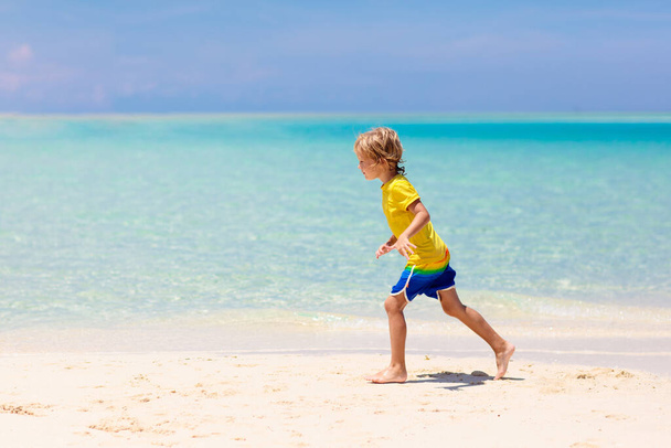 Niños jugando en la playa tropical. Los niños nadan y juegan en el mar en las vacaciones familiares de verano. Diversión de arena y agua, protección solar para niños pequeños. Niño y niña corriendo y saltando en la orilla del océano. - Foto, imagen