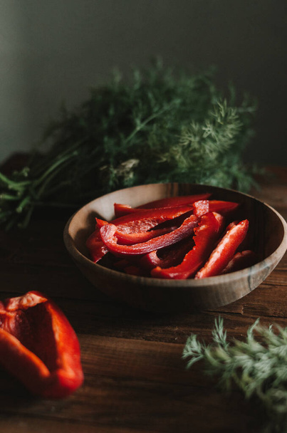 Bright sweet red peppers in the plate among green dill on wooden rustic table on dark background in the kitchen. Delicious ripe vegetables ready to cook close up. Ingridients for hungurian lecho. - Fotografie, Obrázek