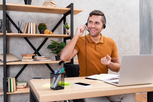 joyful man in headset working at home neat laptop and smartphone with blank screen - Zdjęcie, obraz