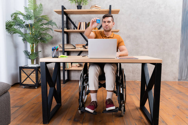 handicapped man showing cube with disability symbol while working in home office - Φωτογραφία, εικόνα