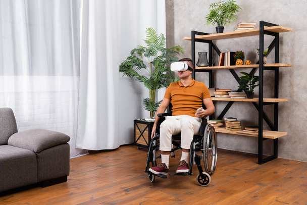 young handicapped man holding mobile phone while gaming in vr headset at home - Photo, Image