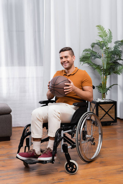 joyful handicapped man holding basketball while sitting in wheelchair - Photo, image