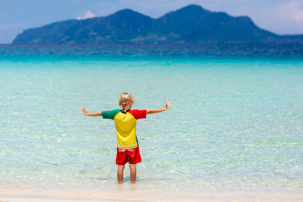 熱帯のビーチで遊んでいる子供たち。子供たちは夏休みに海で泳いだり遊んだりします。砂と水の楽しさ、幼い子供のための太陽の保護。小さな男の子と女の子が走って海の海岸でジャンプします. - 写真・画像