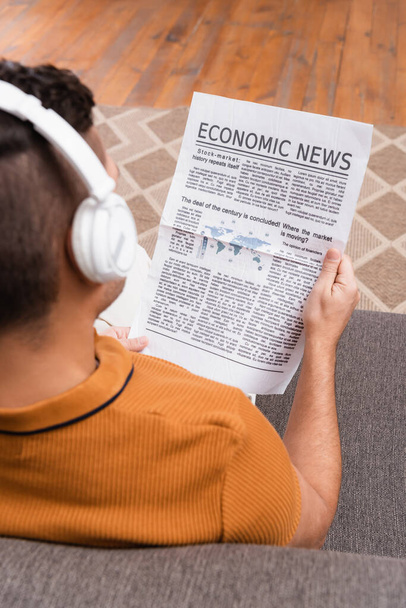 vue aérienne de l'homme dans les écouteurs sans fil lisant les nouvelles économiques sur le premier plan flou - Photo, image