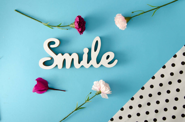 Optimistische Frühlingsausrichtung. Lächelndes Schild mit rosa und weißen Blumen auf pastellblauem Bankett. Minimale kreative flache Lage. - Foto, Bild