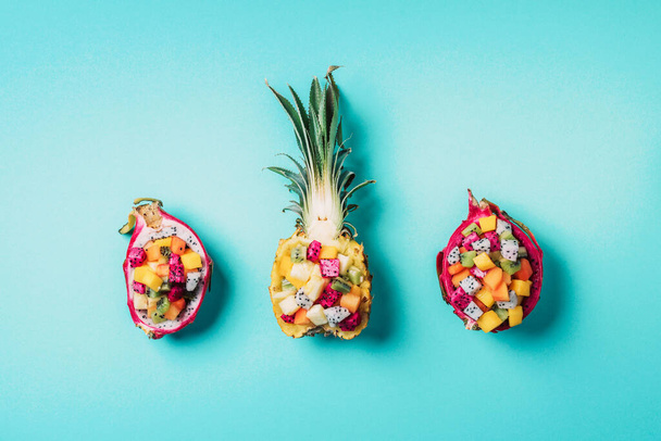 Exotic fruit salad served in half of dragon fruit and pineapple fruit on blue background. Copy space. Tropical travel, exotic fruit. Vegan and vegetarian concept. - Φωτογραφία, εικόνα