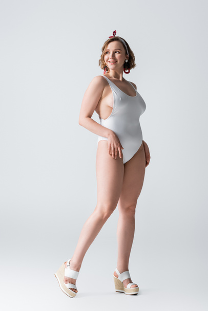 full length of happy overweight young woman in swimwear and earrings posing on white - Фото, зображення