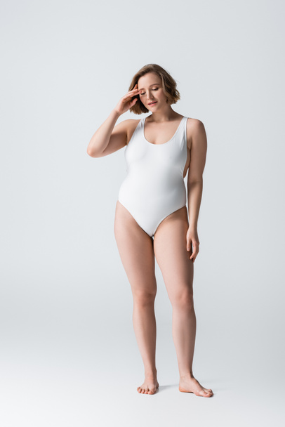 full length of pensive overweight woman in swimsuit standing on white - Фото, зображення
