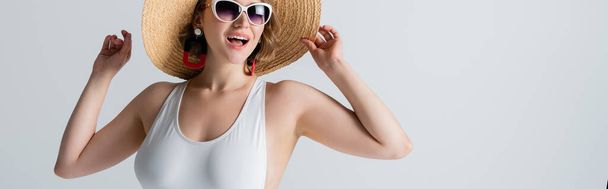 femme en surpoids et joyeuse en lunettes de soleil et maillot de bain ajustant chapeau de paille isolé sur blanc, bannière - Photo, image