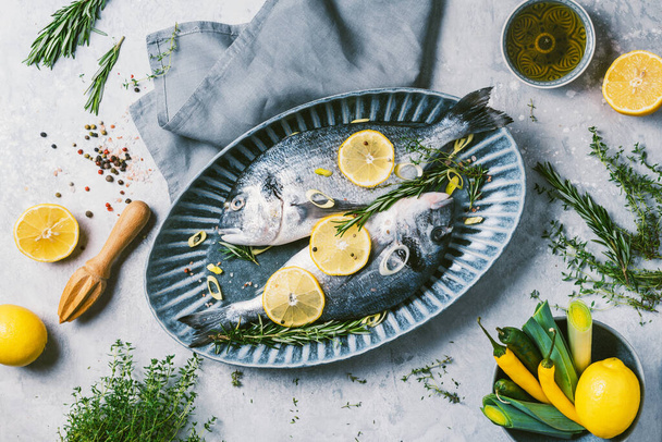 Seafood concept. Cooking dorado or sea bream fish with lemon, herbs, oil, vegetables and spices on concrete background. Top view. Healthy food concept. Copy space. Food pattern - Zdjęcie, obraz