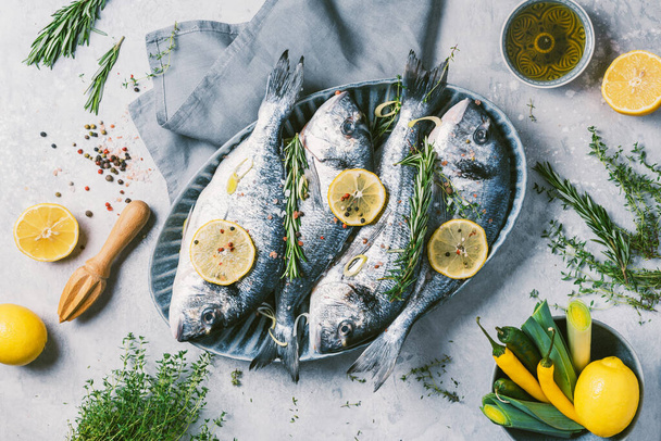 Cooking dorado or sea bream fish with lemon, herbs, oil, vegetables and spices on concrete background. Seafood concept. Top view. Healthy food concept. Copy space. Food pattern - Photo, image