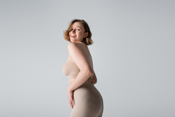 smiling overweight young woman in underwear posing isolated on grey - Photo, Image