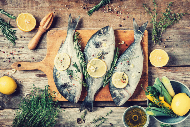 Raw dorado fish with ingredients, lemon, herbs, oil, vegetables and spices on wooden cutting board over wood background. Top view. Healthy food diet. Food pattern. Seafood concept. - Фото, изображение