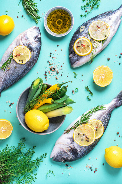 Fresh raw sea dorado fish with lemon slices, herbs, oil, salt, pepper, greens on blue background. Top view. Healthy food concept. Copy space. Food pattern - Zdjęcie, obraz