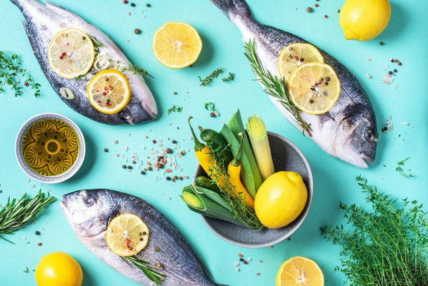 Fresh raw sea dorado fish with lemon slices, herbs, oil, salt, pepper, greens on blue background. Top view. Healthy food concept. Copy space. Food pattern - Fotoğraf, Görsel