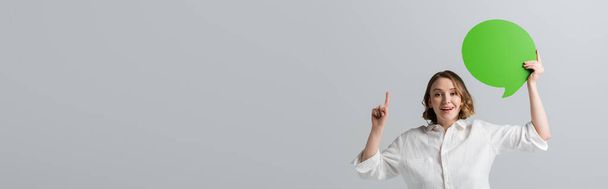 happy overweight woman in white shirt holding green speech bubble and pointing with finger isolated on grey, banner - Fotografie, Obrázek