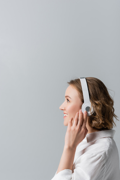 side view of happy plus size woman in wireless headphones listening music isolated on grey - Foto, Imagen