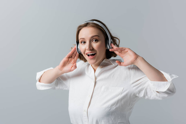 amazed plus size woman in wireless headphones listening music isolated on grey - Фото, изображение