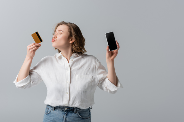 プラスサイズの女性がクレジットカードを持っているとグレーに隔離されたスマートフォンにキス - 写真・画像