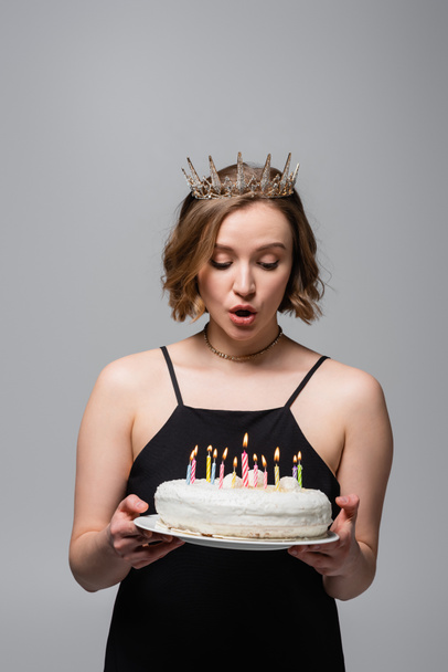 surprised plus size woman in slip dress and crown holding birthday cake isolated on grey  - Valokuva, kuva