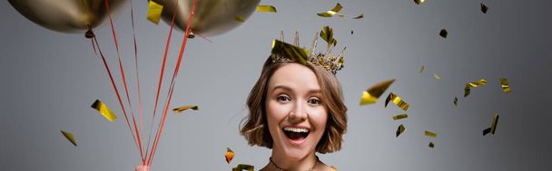 happy plus size woman in crown holding balloons near confetti on grey, banner - Foto, afbeelding