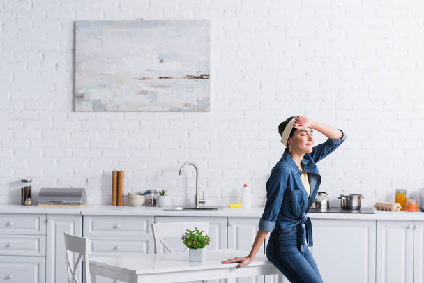 Housewife in denim shirt standing with closed eyes near table  - Photo, Image
