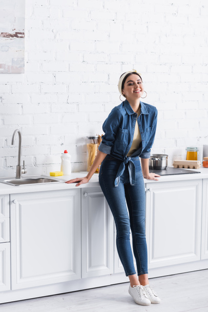 Positive housewife standing near kitchen worktop  - Foto, imagen