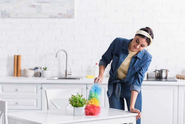 Junge Frau im Jeanshemd putzt Tisch mit Staubbürste  - Foto, Bild