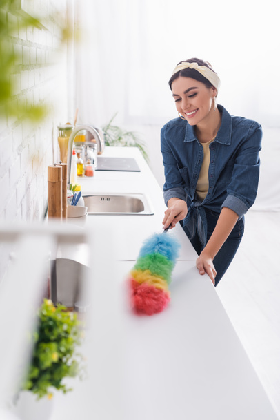 Cheerful housewife cleaning kitchen worktop with dust brush  - Foto, afbeelding