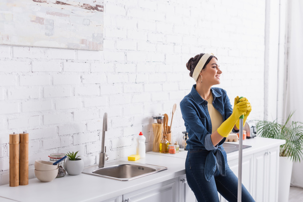 Young smiling woman with mop standing near kitchen worktop  - Photo, Image