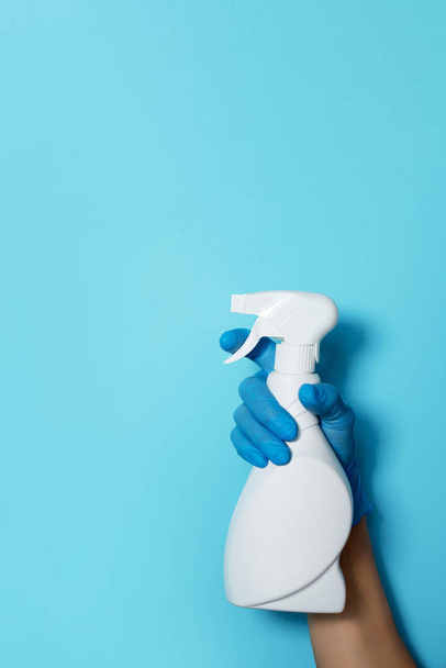 Hand in glove holding white plastic bottle of cleaning product, household chemicals. Copy space. Cleaning service concept. Household chemical cleaning products, brushes and supplies. Detergent bottle - 写真・画像