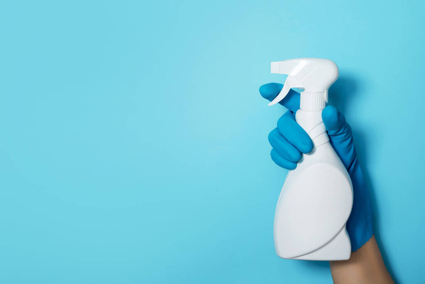 Hand in glove holding white plastic bottle of cleaning product, household chemicals. Copy space. Cleaning service concept. Household chemical cleaning products, brushes and supplies. Detergent bottle - Photo, image