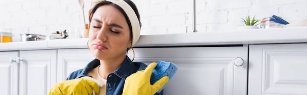 Triste ama de casa sosteniendo esponja y detergente cerca de encimera de cocina, pancarta   - Foto, imagen