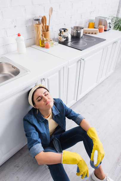 Femme au foyer fatiguée avec détergent et éponge assise sur le sol de la cuisine  - Photo, image