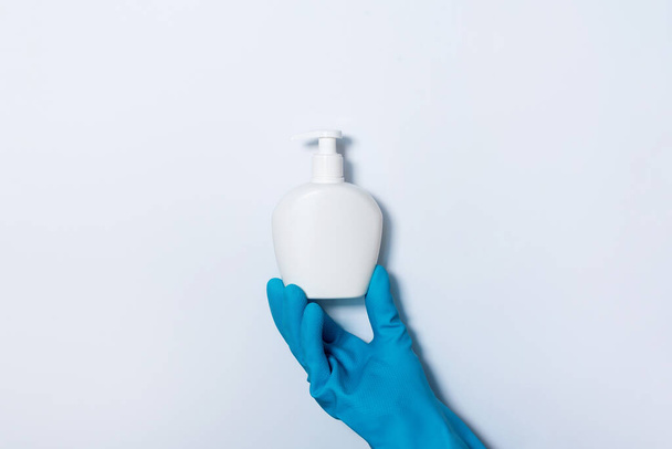 Hand in glove holding soap bottle and medical face mask on white background. Copy space. Preventive measures to protect against coronavirus. Products to stay safe during pandemic covid19 quarantine. - Fotó, kép