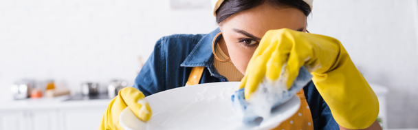 Женщина в резиновых перчатках моет тарелку на размытом переднем плане, баннер  - Фото, изображение