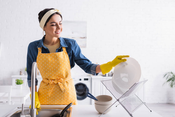 Mujer feliz en delantal poner plato en pie en la cocina  - Foto, Imagen
