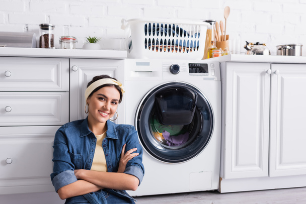 Sorridente casalinga guardando la macchina fotografica vicino alla lavatrice in cucina  - Foto, immagini