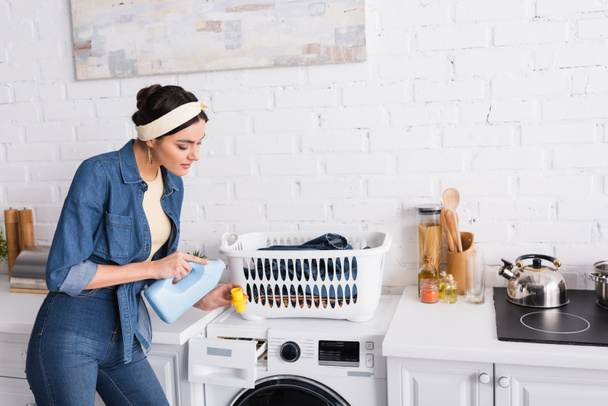 Housewife holding detergent near washing machine and clothes  - Photo, Image